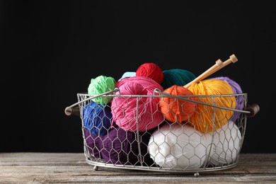 Photo of Many soft skeins of yarn and knitting needles in metal basket on wooden table