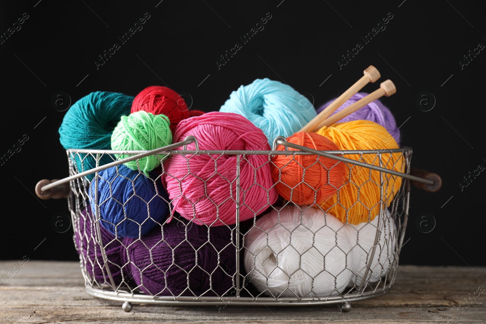 Photo of Many soft skeins of yarn and knitting needles in metal basket on wooden table