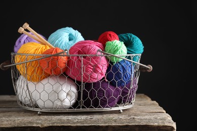 Many soft skeins of yarn and knitting needles in metal basket on wooden table