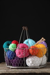 Photo of Many soft skeins of yarn and knitting needles in metal basket on wooden table