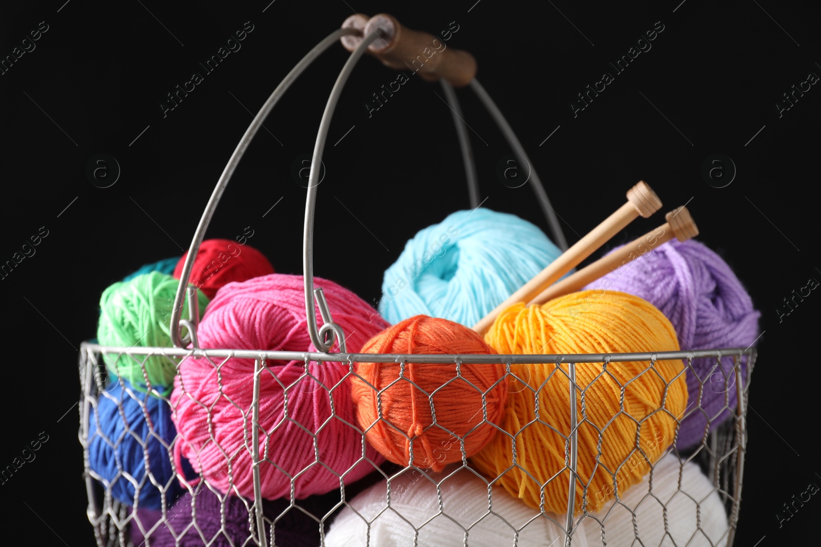 Photo of Many soft skeins of yarn in metal basket on black background, closeup