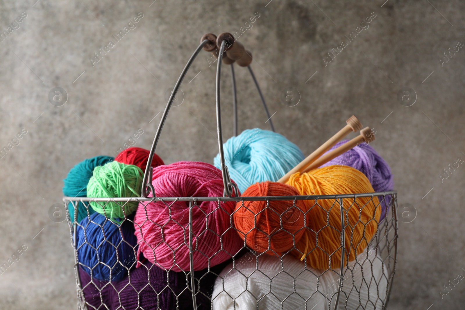 Photo of Many soft skeins of yarn and knitting needles in metal basket on grey background, closeup