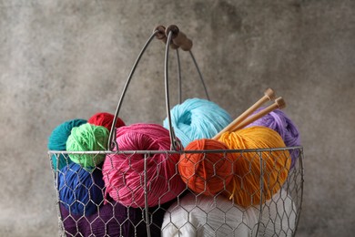 Photo of Many soft skeins of yarn and knitting needles in metal basket on grey background, closeup