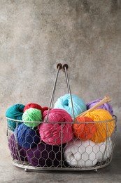 Many soft skeins of yarn and knitting needles in metal basket on grey background