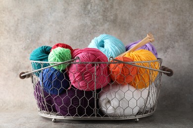 Photo of Many soft skeins of yarn and knitting needles in metal basket on grey background