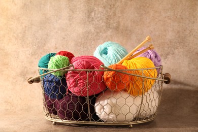 Photo of Many soft skeins of yarn and knitting needles in metal basket on light brown background