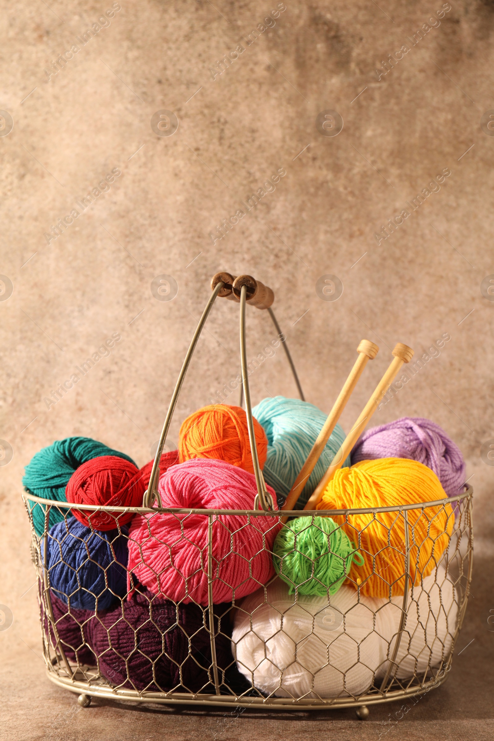 Photo of Many soft skeins of yarn and knitting needles in metal basket on light brown background, space for text