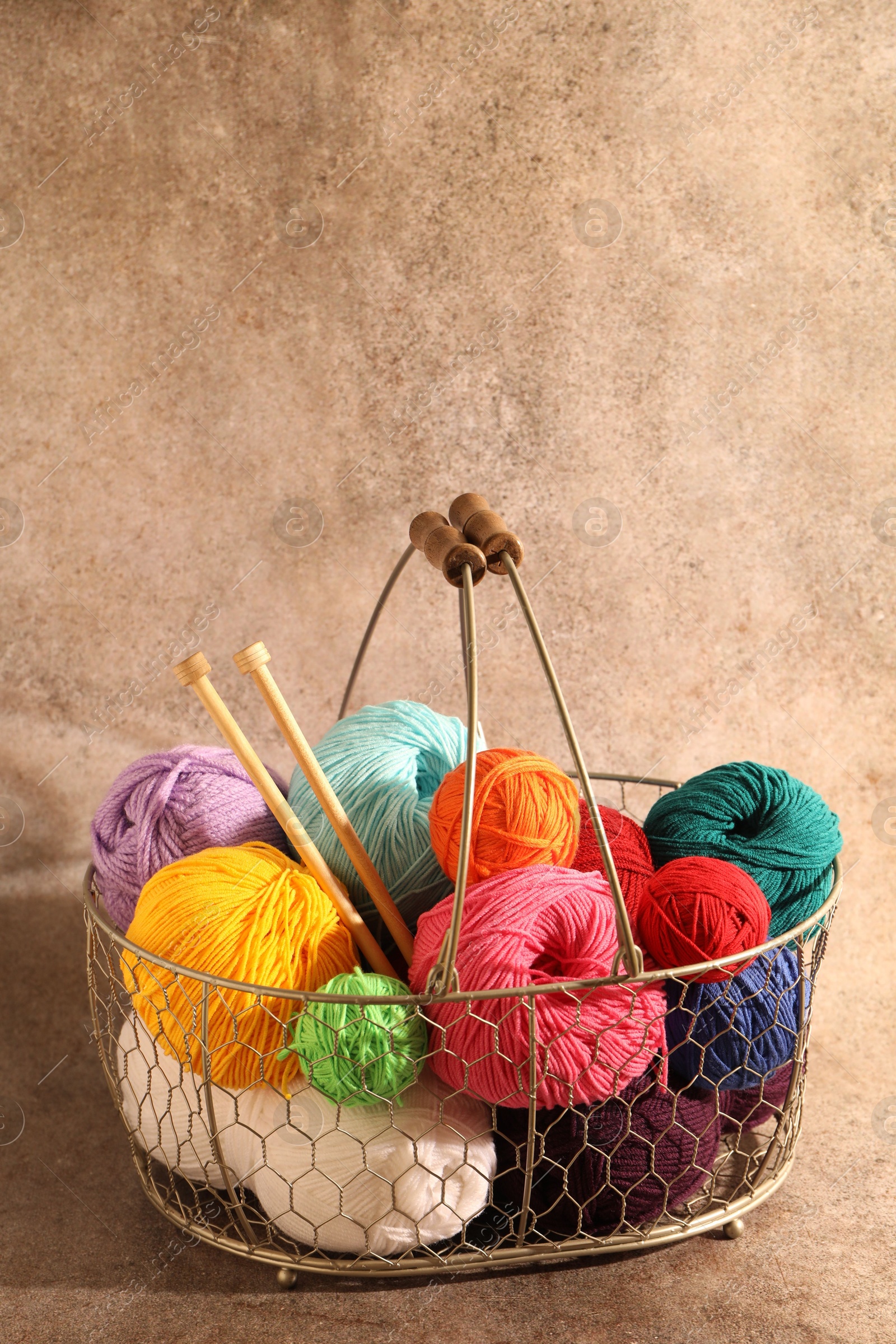 Photo of Many soft skeins of yarn and knitting needles in metal basket on light brown background, space for text