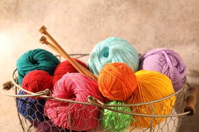 Photo of Many soft skeins of yarn and knitting needles in metal basket on light brown background, closeup