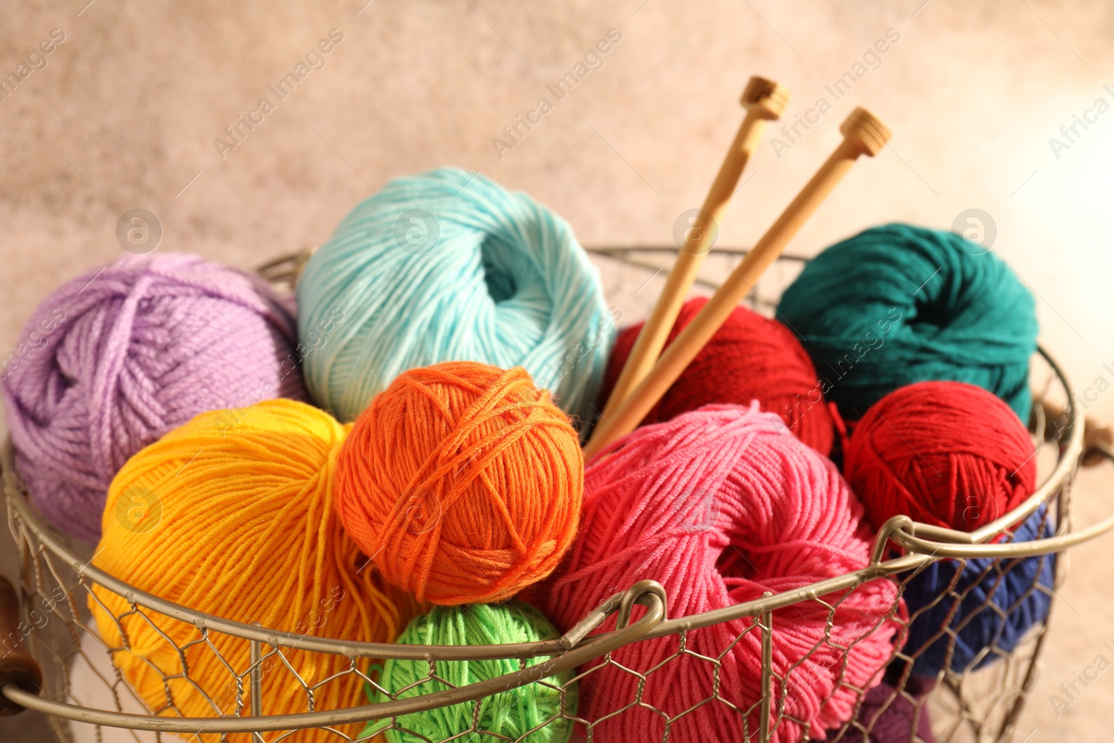 Photo of Many soft skeins of yarn and knitting needles in metal basket on light brown background, closeup