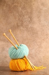 Photo of Two soft skeins of yarn and knitting needles on light brown background, space for text