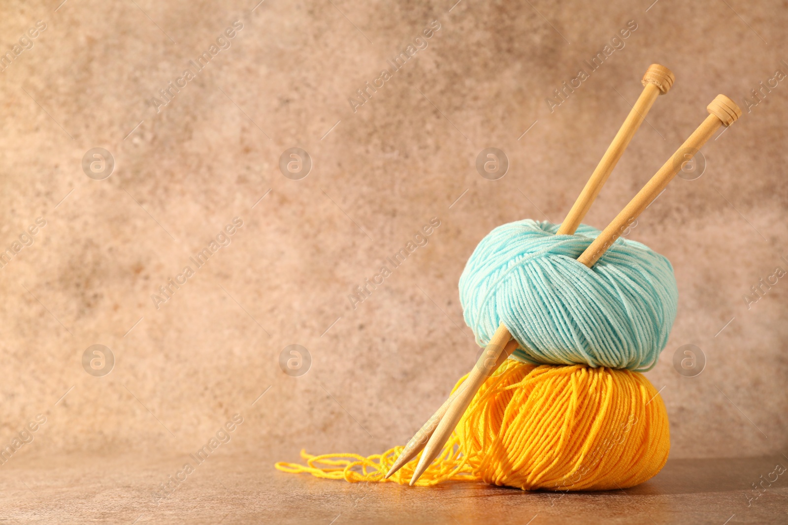 Photo of Two soft skeins of yarn and knitting needles on light brown background, space for text