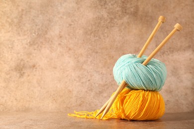 Photo of Two soft skeins of yarn and knitting needles on light brown background, space for text