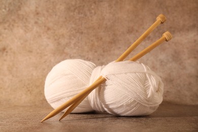 Photo of White soft skein of yarn and knitting needles on light brown background