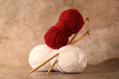 Two soft skeins of yarn and knitting needles on light brown background