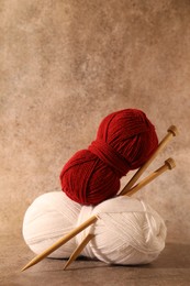 Two soft skeins of yarn and knitting needles on light brown background