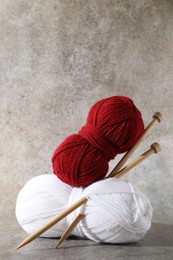 Two soft skeins of yarn and knitting needles on grey background