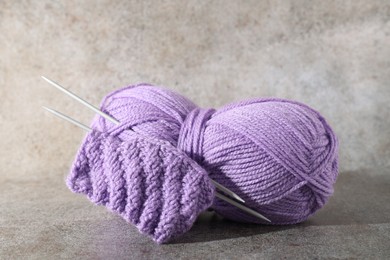 Photo of Skein of violet yarn, knitted fabric and needles on grey background