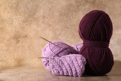 Photo of Skeins of yarn, knitted fabric and needles on light brown background, space for text