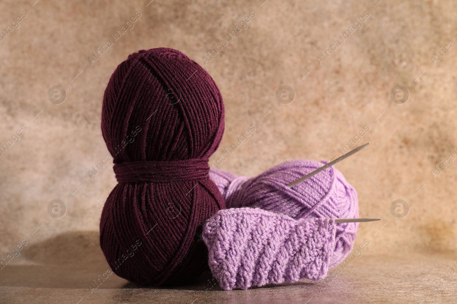 Photo of Skeins of yarn, knitted fabric and needles on light brown background