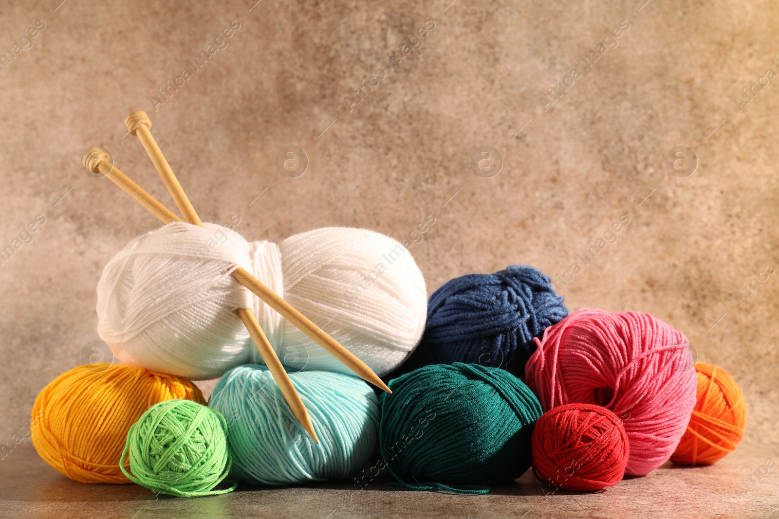 Photo of Many soft skeins of yarn and knitting needles on light brown background, space for text