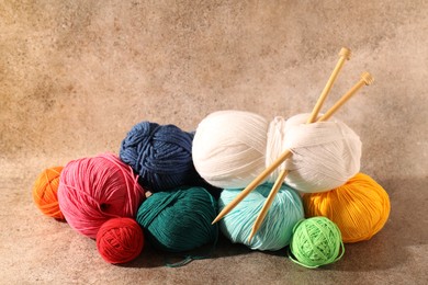 Many soft skeins of yarn and knitting needles on light brown background, space for text