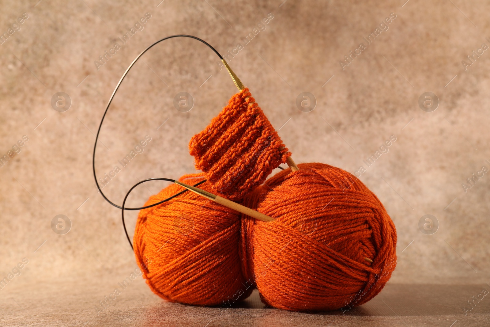 Photo of Skein of orange yarn, knitted fabric and needles on light brown background