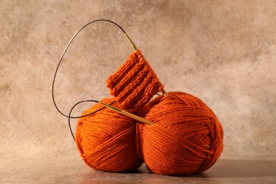 Photo of Skein of orange yarn, knitted fabric and needles on light brown background