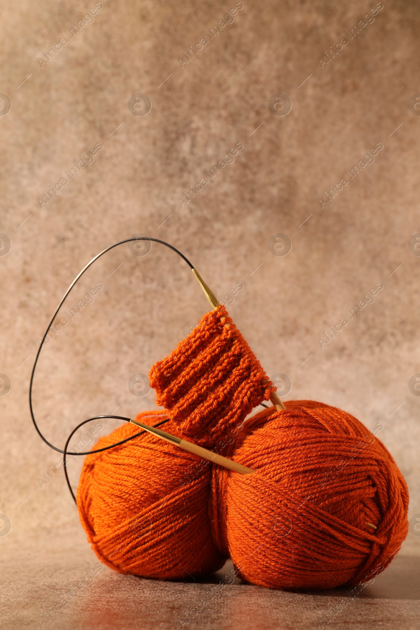 Photo of Skein of orange yarn, knitted fabric and needles on light brown background, space for text