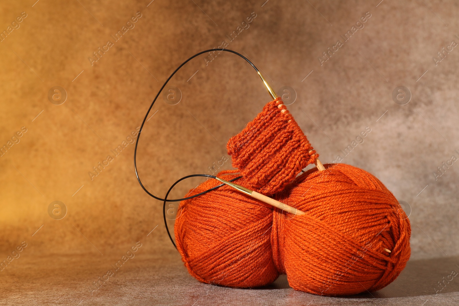 Photo of Skein of orange yarn, knitted fabric and needles on light brown background, space for text