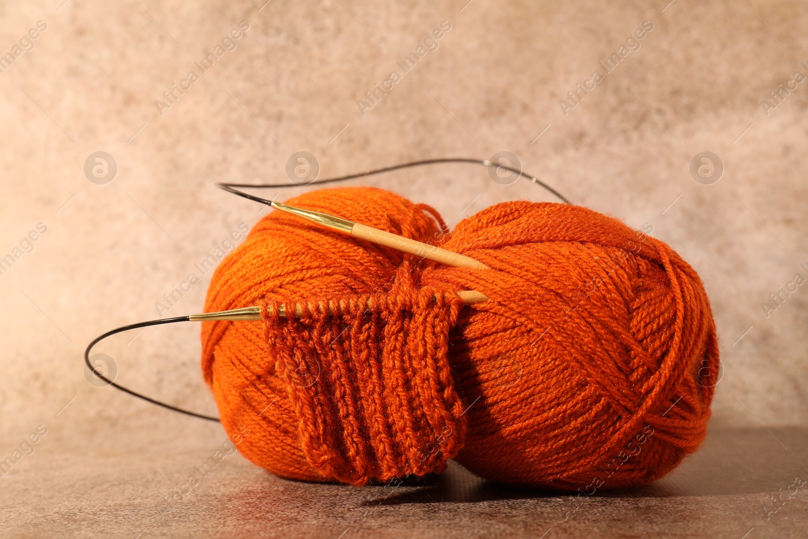 Photo of Skein of orange yarn, knitted fabric and needles on light brown background