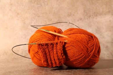 Photo of Skein of orange yarn, knitted fabric and needles on light brown background