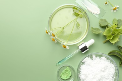 Photo of Petri dishes with leaves, chamomile flowers and cosmetic products on green background, flat lay. Space for text