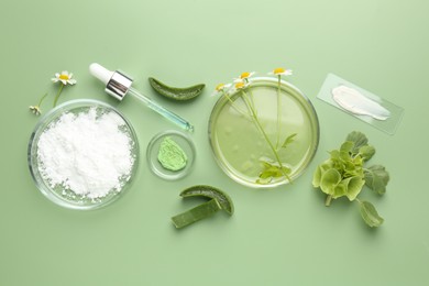 Petri dishes with leaves, chamomile flowers and cosmetic products on green background, flat lay