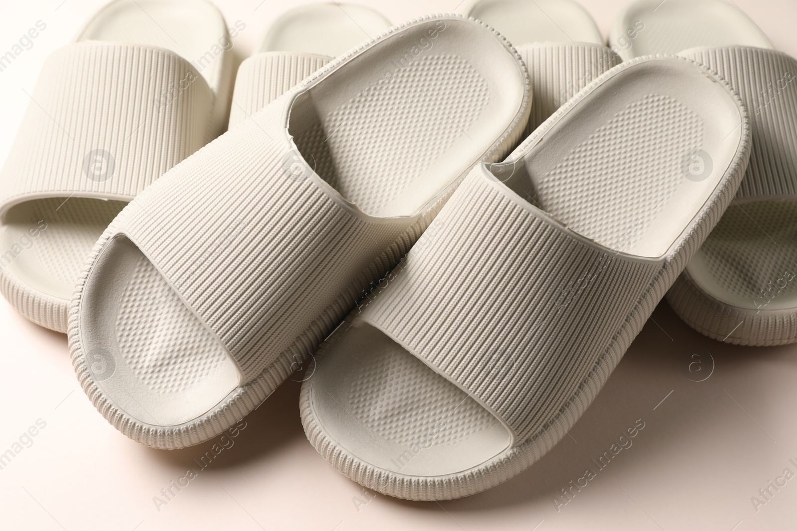 Photo of Pairs of rubber slippers on beige background, closeup