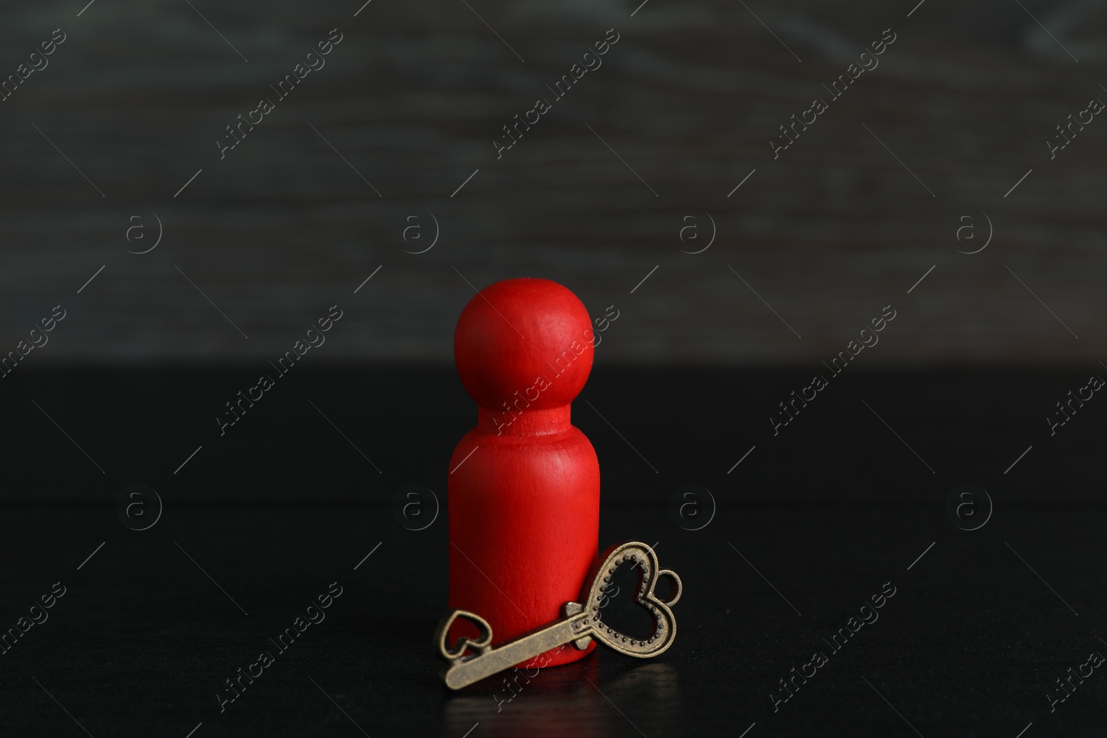 Photo of Red human figure and key on black wooden table, closeup