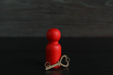 Photo of Red human figure and key on black wooden table, closeup