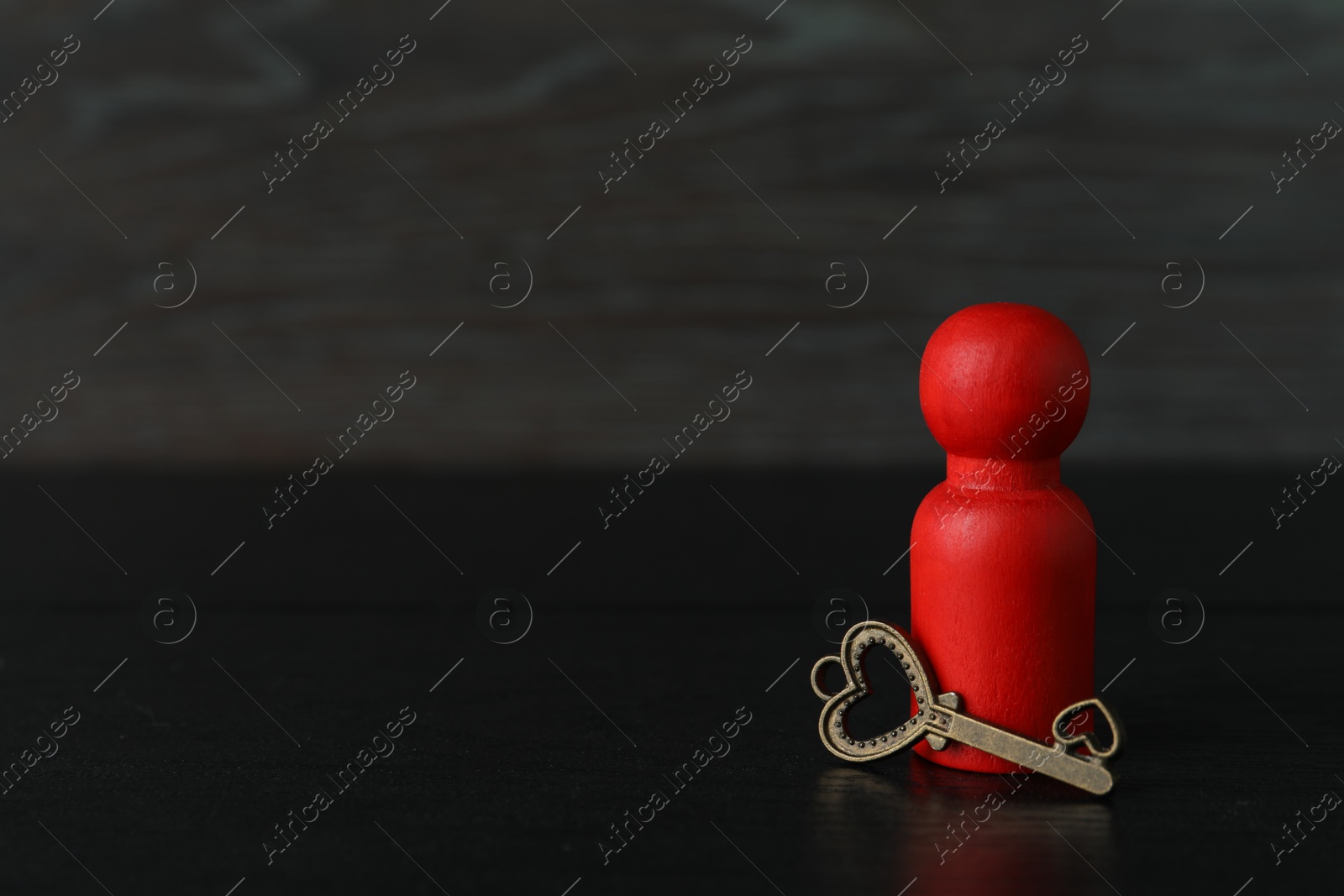 Photo of Red human figure and key on black wooden table, closeup. Space for text