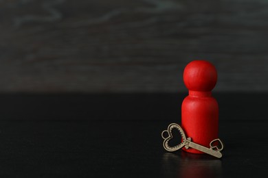 Photo of Red human figure and key on black wooden table, closeup. Space for text