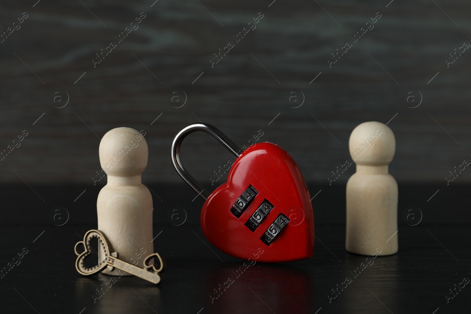 Photo of Wooden human figures with lock in shape of heart and key on black table, closeup