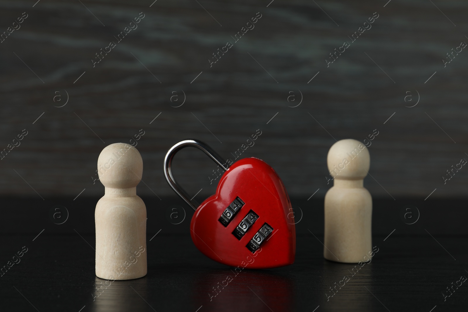 Photo of Wooden human figures and lock in shape of heart on black table, closeup