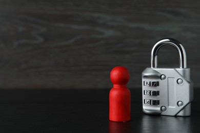 Photo of Red human figure and metal lock on black wooden table, closeup. Space for text