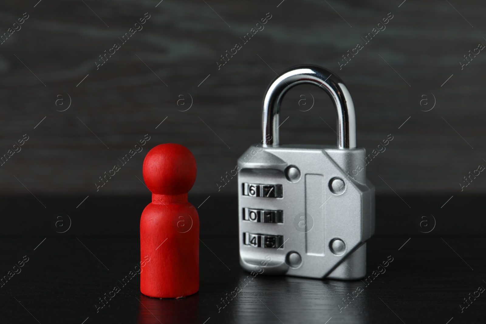 Photo of Red human figure and metal lock on black wooden table, closeup