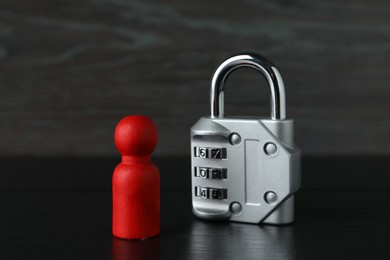 Photo of Red human figure and metal lock on black wooden table, closeup