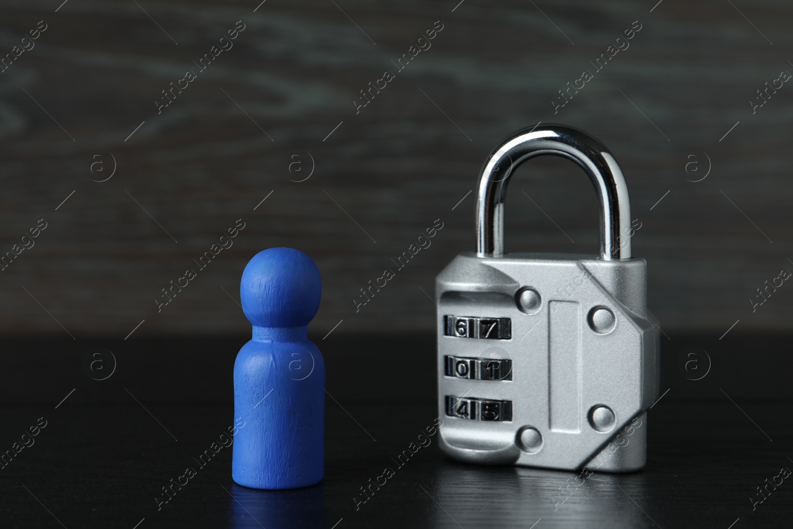 Photo of Blue human figure and metal lock on black wooden table, closeup