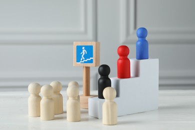 Photo of Stairs with group of different wooden human figures and road sign on white table