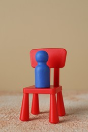 Photo of Blue human figure on chair against beige background, closeup