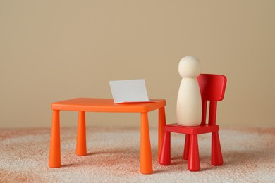 Wooden human figure on chair at table against beige background