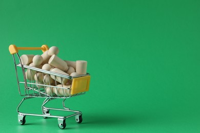 Photo of Wooden human figures in small shopping cart on green background, space for text