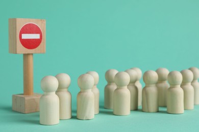 Wooden human figures and No entry road sign on turquoise background